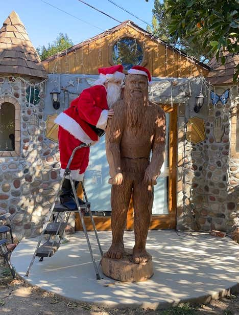 Santa Claus standing on a ladder to whisper something to Bigfoot